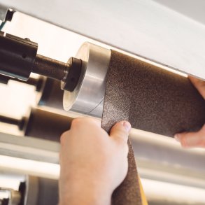 Technician applying self-adhesive cork rubber roller covering tape spirally on an industrial steel roller by Nova Beltech