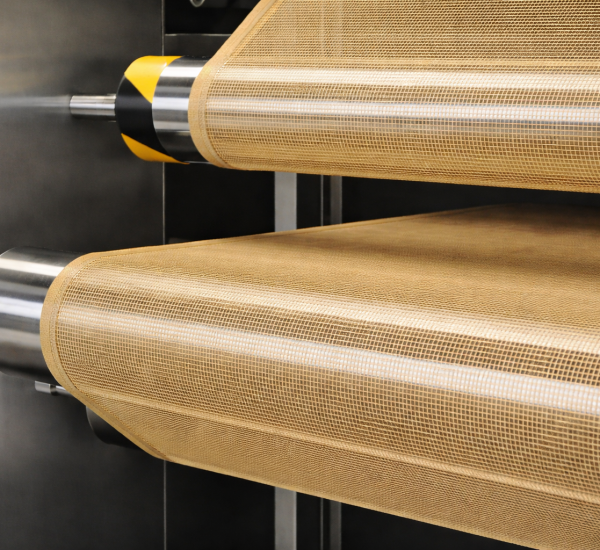 PTFE coated open mesh conveyor belt running on stainless steel rollers in heat drying system by Nova Beltech